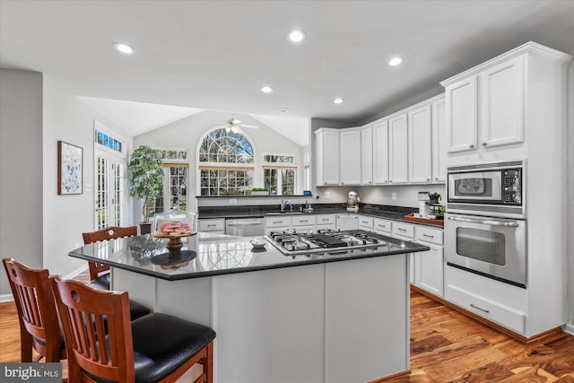 kitchen featuring light wood finished floors, stainless steel appliances, dark countertops, white cabinets, and lofted ceiling
