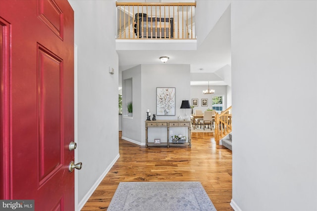 entryway featuring wood finished floors, an inviting chandelier, a healthy amount of sunlight, baseboards, and a high ceiling