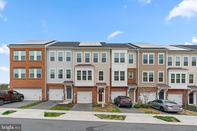 townhome / multi-family property featuring driveway, an attached garage, brick siding, roof mounted solar panels, and a residential view