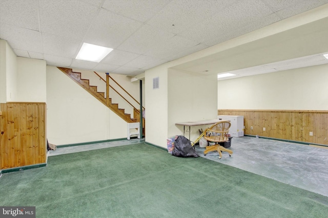 finished below grade area with wooden walls, a paneled ceiling, stairway, and a wainscoted wall
