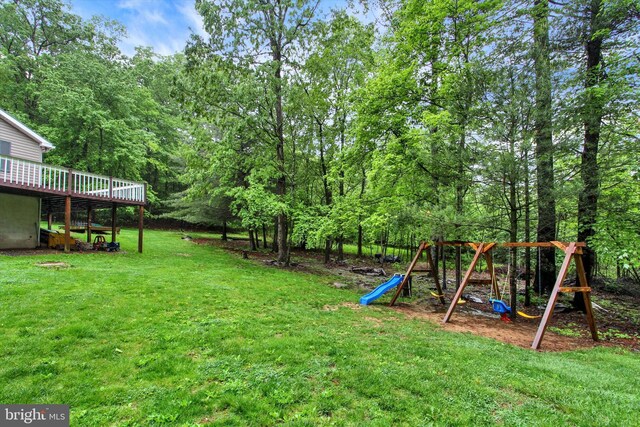 view of grassy yard featuring a playground and a wooden deck