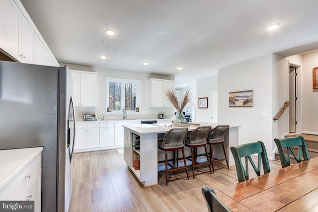 kitchen featuring white cabinetry, a kitchen island, stainless steel fridge, and a breakfast bar
