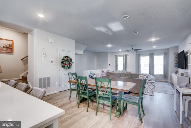 dining space with visible vents, light wood finished floors, baseboards, stairs, and a ceiling fan