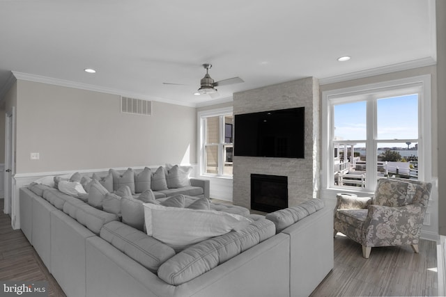 living room with light wood-type flooring, a ceiling fan, ornamental molding, and visible vents