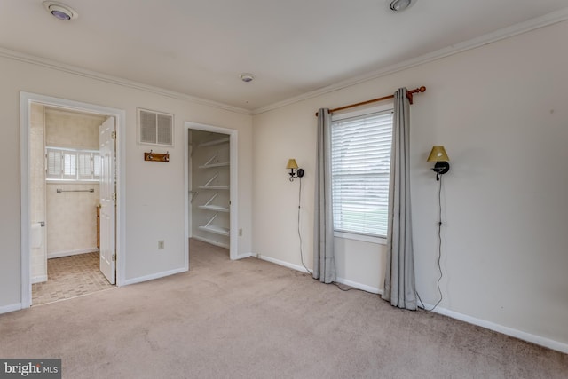 unfurnished bedroom with carpet flooring, ornamental molding, a walk in closet, and visible vents