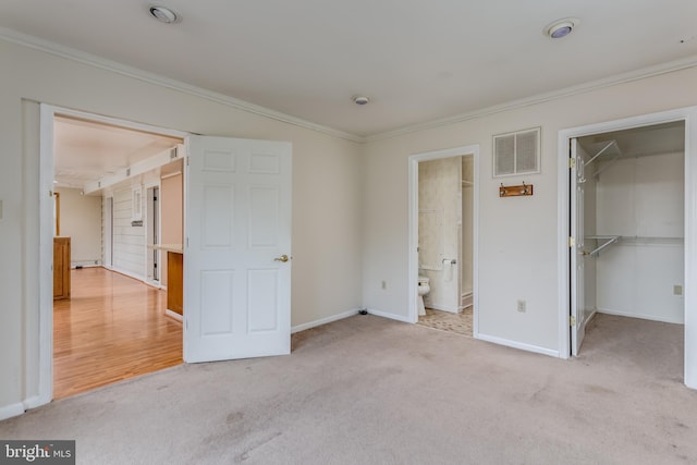 unfurnished bedroom featuring crown molding, a spacious closet, carpet, baseboards, and visible vents