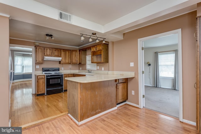 kitchen with under cabinet range hood, range with gas stovetop, a sink, visible vents, and a peninsula
