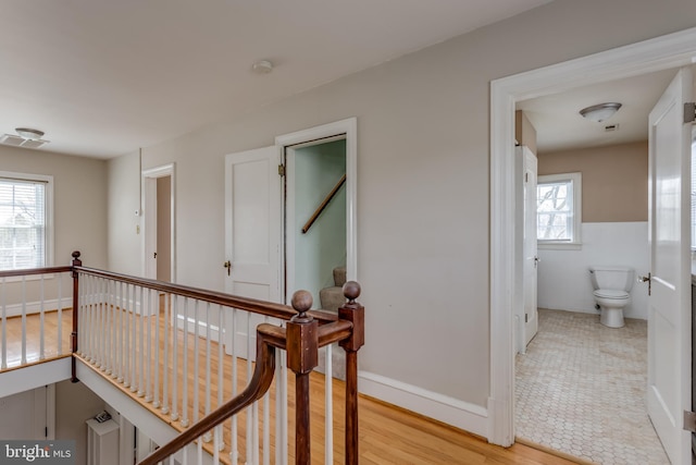 hallway featuring light wood-style flooring, visible vents, an upstairs landing, and tile walls