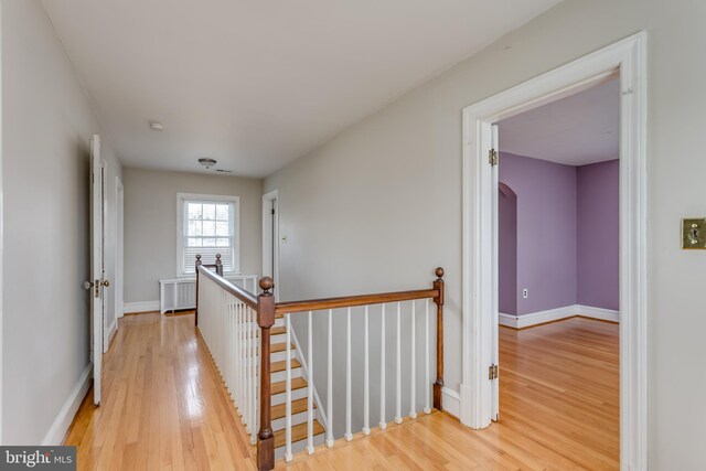 corridor with an upstairs landing, wood finished floors, radiator, baseboards, and arched walkways