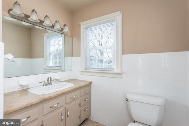 bathroom featuring toilet, vanity, tile walls, and wainscoting