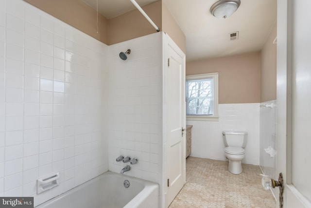 full bathroom featuring a wainscoted wall, toilet, shower / bathing tub combination, visible vents, and tile walls