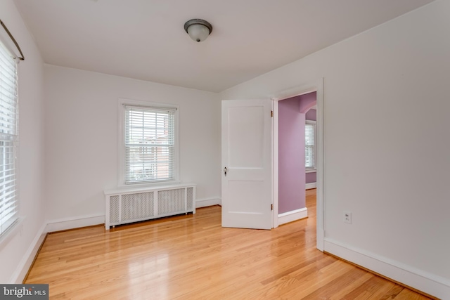 spare room with baseboards, light wood-type flooring, and radiator