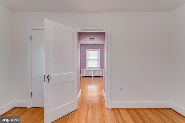 hallway featuring radiator, light wood-type flooring, arched walkways, and baseboards