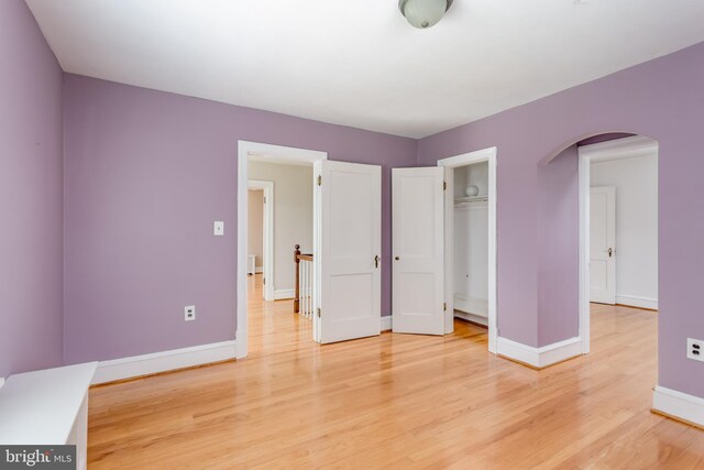 unfurnished bedroom featuring arched walkways, baseboards, a closet, and light wood finished floors