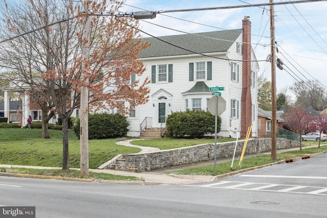 view of front of home featuring a shingled roof, a chimney, and a front yard