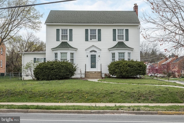 colonial-style house with a chimney, a shingled roof, a front lawn, and entry steps