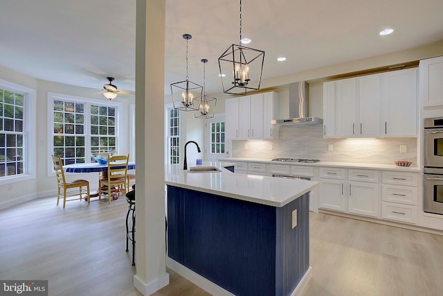 8177 Bodkin Ave, Pasadena, MD 21122 - kitchen with wall chimney range hood, backsplash, appliances with stainless steel finishes, a sink, and light wood-style flooring