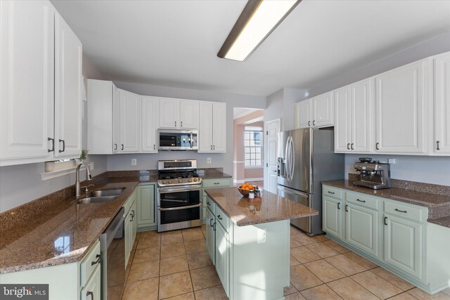 kitchen with white cabinets, stainless steel appliances, a sink, and dark stone countertops