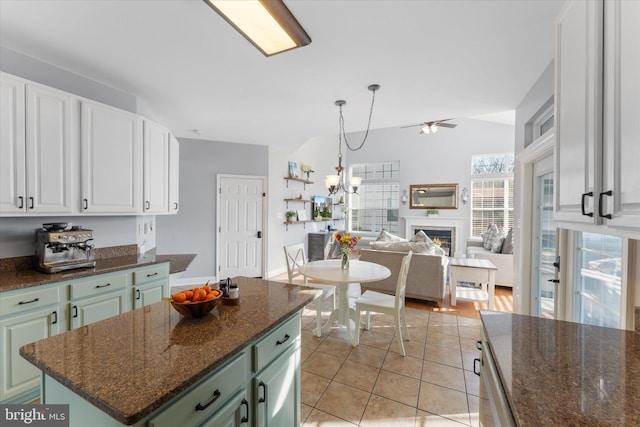 kitchen with white cabinets, open floor plan, ceiling fan with notable chandelier, green cabinets, and a warm lit fireplace