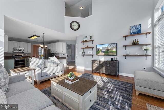 living room featuring dark wood finished floors, a high ceiling, baseboards, and a notable chandelier