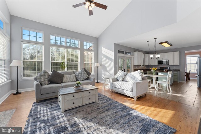 living room featuring high vaulted ceiling, wood finished floors, baseboards, and ceiling fan with notable chandelier