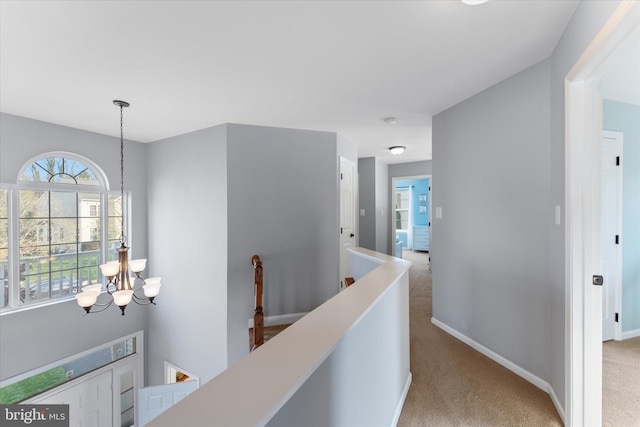 hall with a notable chandelier, light carpet, baseboards, and an upstairs landing