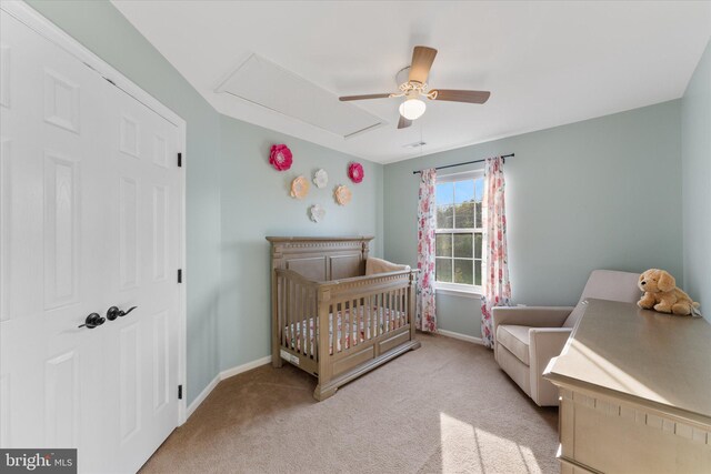 bedroom featuring a crib, baseboards, attic access, carpet flooring, and ceiling fan