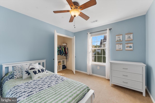 bedroom with visible vents, light carpet, a walk in closet, baseboards, and ceiling fan