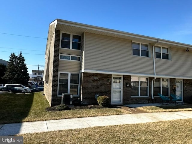 view of property with brick siding, a front yard, and central AC unit