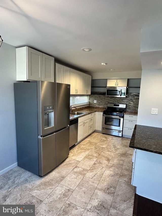 kitchen with a sink, stainless steel appliances, baseboards, decorative backsplash, and dark stone counters