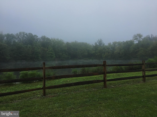 view of yard featuring a rural view, a wooded view, and fence