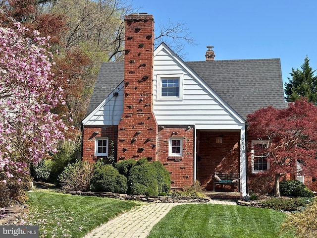 rear view of house featuring a chimney, a yard, brick siding, and a shingled roof