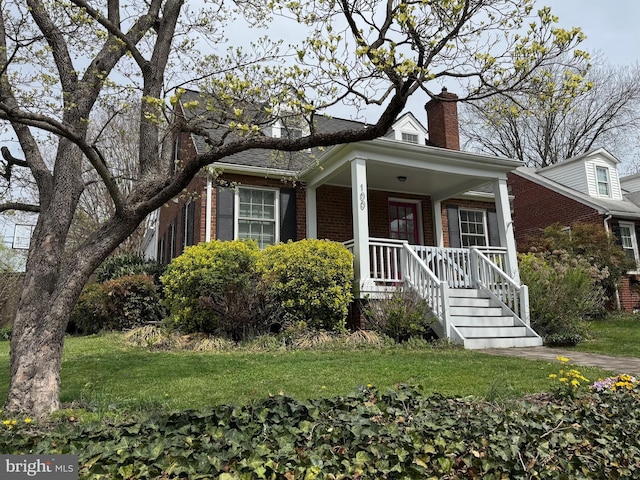 view of front facade with brick siding, a porch, a chimney, and a front lawn