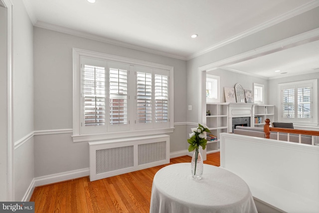 living area featuring baseboards, a fireplace, crown molding, radiator, and wood finished floors