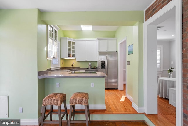 kitchen featuring stainless steel fridge, a peninsula, glass insert cabinets, white cabinetry, and light wood-style flooring