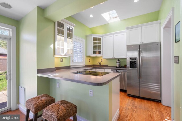 kitchen with a sink, a wealth of natural light, white cabinetry, stainless steel appliances, and a skylight
