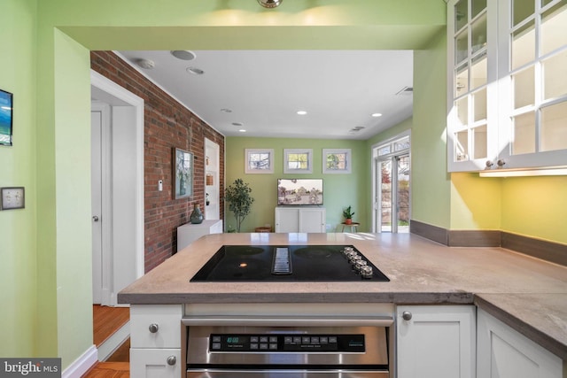kitchen with glass insert cabinets, wall oven, white cabinets, brick wall, and black electric cooktop
