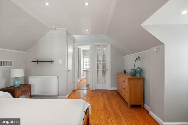 bedroom with light wood finished floors, visible vents, vaulted ceiling, and radiator
