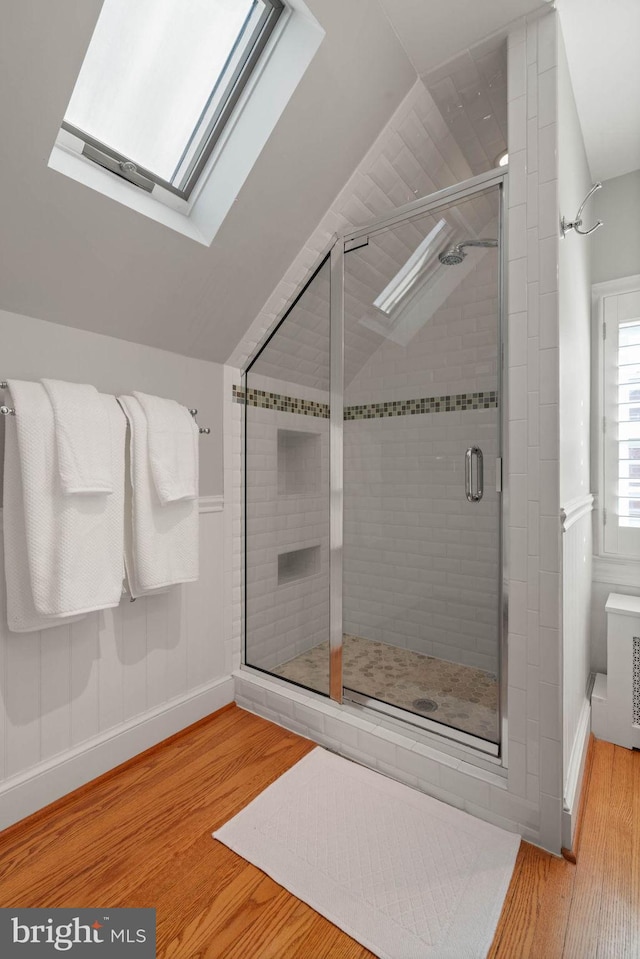 bathroom with baseboards, wood finished floors, a stall shower, and lofted ceiling with skylight