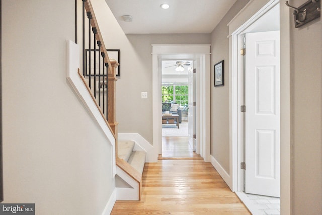 entryway with baseboards, ceiling fan, light wood-style flooring, and stairway