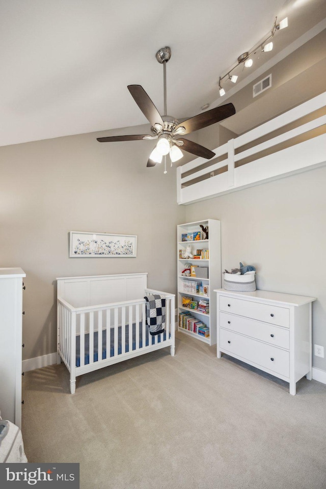 bedroom with visible vents, a nursery area, vaulted ceiling, and light colored carpet