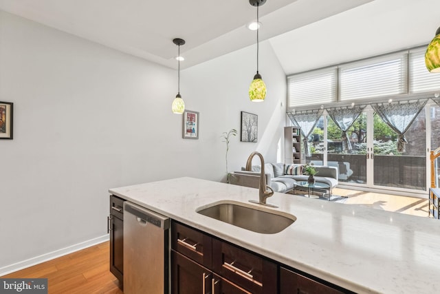 kitchen featuring dishwasher, a sink, light wood-style floors, baseboards, and hanging light fixtures
