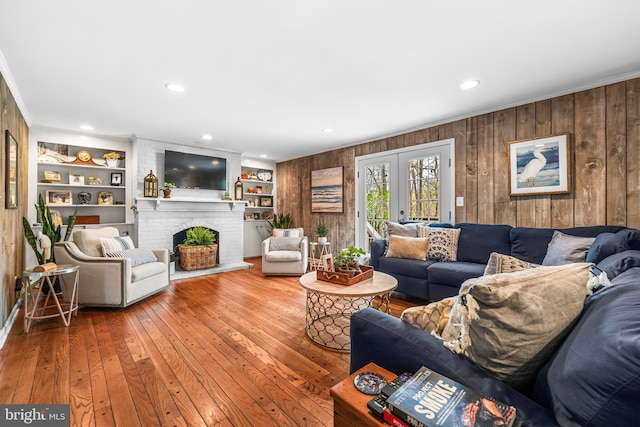 living room featuring crown molding, recessed lighting, hardwood / wood-style floors, a brick fireplace, and wooden walls