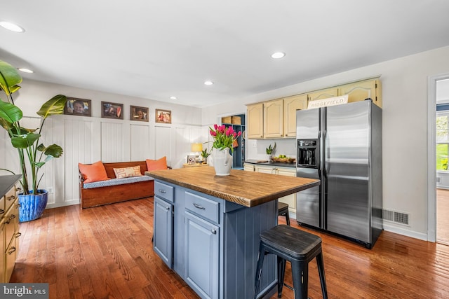 kitchen with hardwood / wood-style floors, stainless steel fridge with ice dispenser, visible vents, and a kitchen island