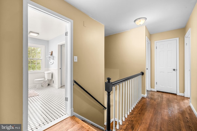 corridor with baseboards, an upstairs landing, and wood finished floors