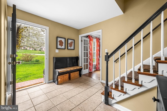foyer entrance with stairs, light tile patterned floors, and baseboards