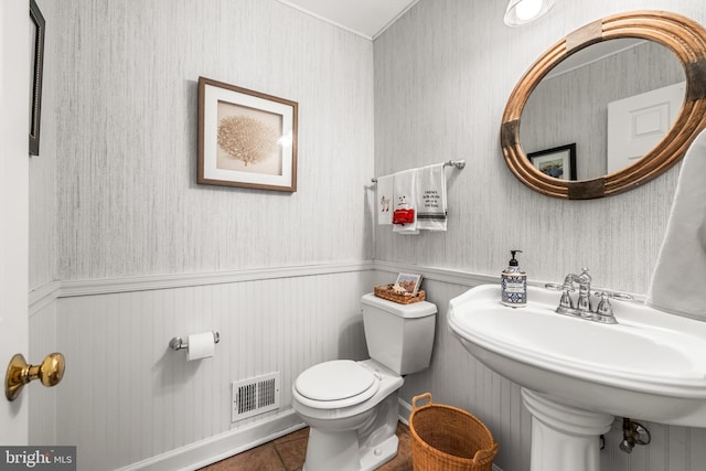 bathroom with tile patterned flooring, visible vents, a wainscoted wall, toilet, and a sink