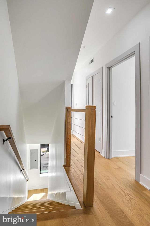 stairs featuring visible vents, baseboards, wood finished floors, and electric panel