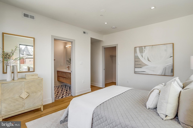 bedroom featuring a walk in closet, ensuite bath, visible vents, and light wood-type flooring