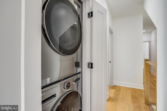 laundry area featuring stacked washer and dryer, baseboards, light wood-type flooring, and laundry area